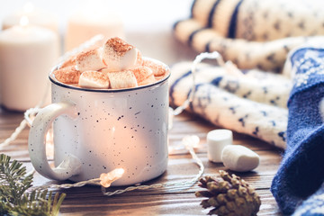 Hot cocoa with marshmallow in a white ceramic mug surrounded by winter things on a wooden table. The concept of cosy holidays and New Year.