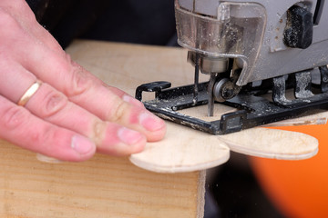 cut out a flower with an electric jigsaw from a plywood sheet, an electric tool and hands of the master of work