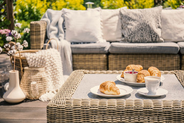 An outdoor wicker table and a sofa with cushions. Croissants for breakfast on a patio on a summer...