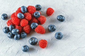 Blueberries and raspberries mix on the background of gray cement. Ripe and juicy fresh raspberries and blueberries close-up. A lot of berries close-up.