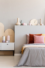 Lamp on bedside cabinet next to bed with colorful cushions in grey bedroom interior. Real photo