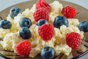 Cottage cheese with fresh raspberries and blueberries in a plate for a healthy breakfast with ripe berries. A natural healthy product.