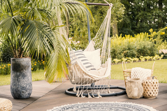 Summer in the green garden with a hammock and a palm tree on a terrace.