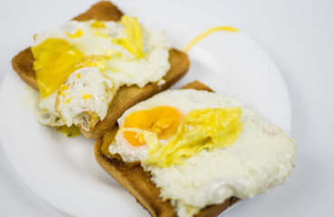 Fried chicken eggs with a burst yolk on toast on a white plate.