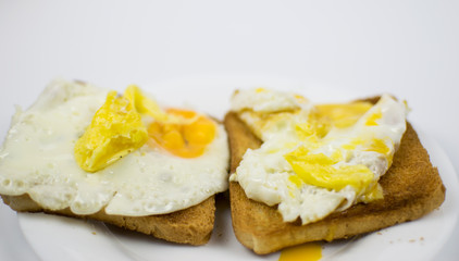 Fried chicken eggs with a burst yolk on toast on a white plate.