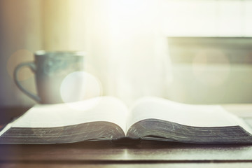 open bible  book with a cup of coffee against window light in the morning, christian devotional