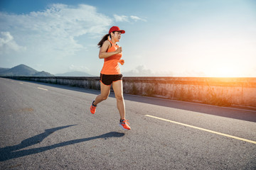 An asian woman athletic is jogging on the concrete road, she is warming her body and tideten her tying her shoes tightly fitting before workout.