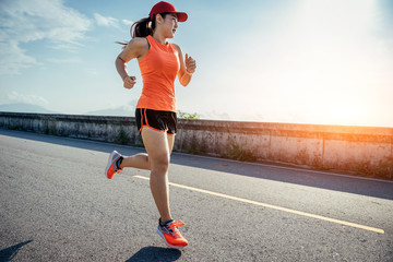 An asian woman athletic is jogging on the concrete road, she is warming her body and tideten her tying her shoes tightly fitting before workout.