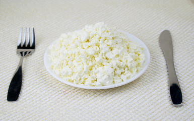 Cottage cheese in a plate with a fork and knife. The concept of healthy food.