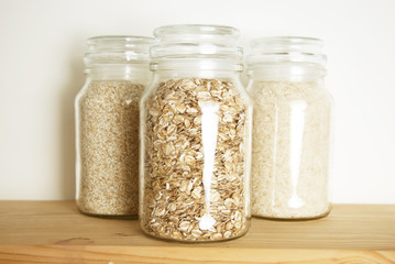 Various uncooked cereals, grains, and pasta for healthy cooking in glass jars on wooden table. Top view. Clean eating, balanced dieting food