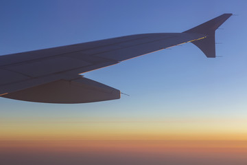 Fototapeta premium Wing of an airplane in the sunset. Airplane wing out of window.