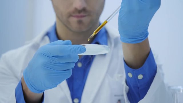 Medical research scientists mixes smoking compounds from tests tube with matter in a petri dish.