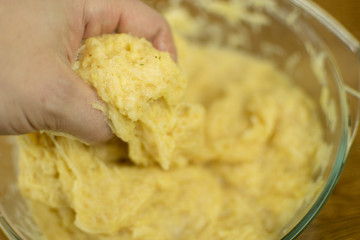 The hand is kneading grated potatoes to make dough.