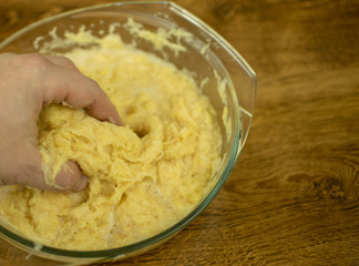 The hand is kneading grated potatoes to make dough.