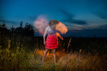 A girl in a black top and red skirt with white cloud arround her hair in a field during photoshoot with flour in sunset