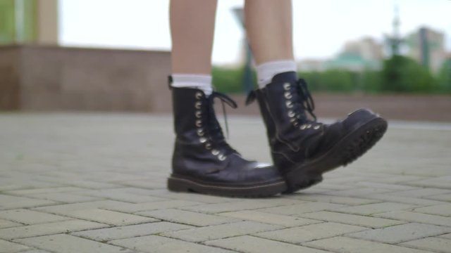 Close shot of female legs walking in heavy armi boots. Closeup shooting fashionable female in leather boots walk in street on stone