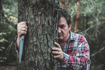maniac with a knife stands behind a tree