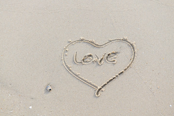 Fototapeta na wymiar Heart and Love written on the beach by the sea in the morning