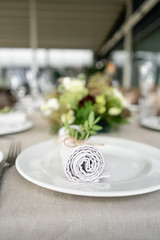 Neatly twisted into a tube dining room napkin decorated with a sprig of pistachio. Wedding Banquet or gala dinner. The chairs and table for guests, served with cutlery and crockery. party on terrace