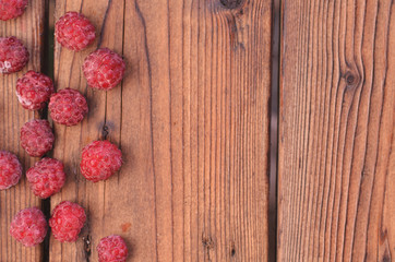 On a wooden background, raspberry is spread out on the left