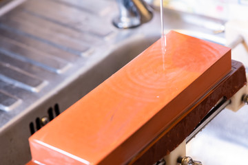 woman professional chef hands hold knife for whetting on whetstone.premium professional stone from japan.knife sharpening process with traditional sharpener stone for knife sharpen edge in restaurant.