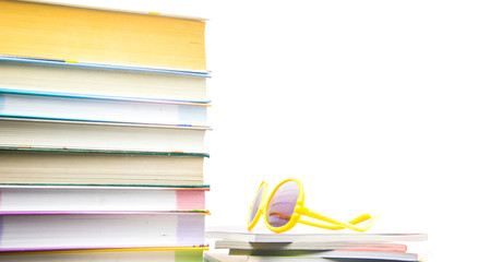 A stack of colorful magazines and books. On the magazines lie yellow sunglasses.