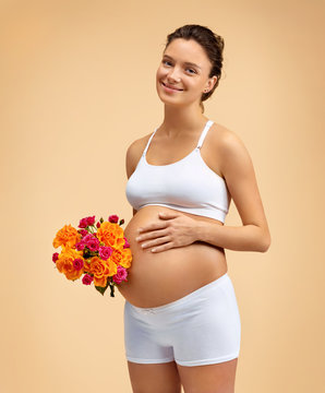 Happy pregnant woman with bouquet of flowers on beige background. Pregnancy, maternity, preparation and expectation concept