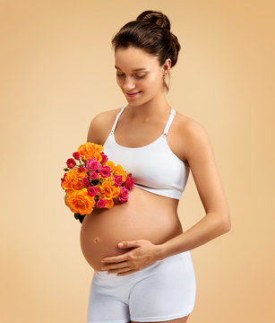 Smiling pregnant woman with bouquet of flowers on beige background. Pregnancy, maternity, preparation and expectation concept