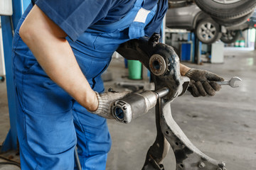Car mechanic inspecting car wheel and repair suspension detail. Lifted automobile at repair service...