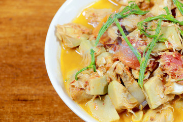 Northern Thailand local food called Kaeng Khanun-on is cooking like a young jack fruit soup with pork spare rib Thai herb, Climbing Wattle, Acacia pennata, red eggplant in white bowl on wooden table.