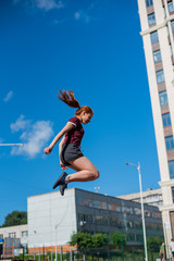 the red-haired student in shorts gives the standards for jumping at the physical education class on an open sports ground. girl doing crossfit exercises outdoor. red-haired young woman is jumping