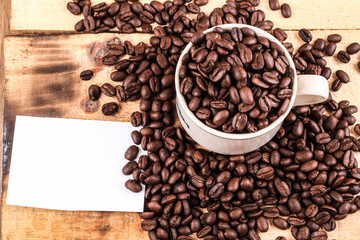 Cup of coffee full of coffee beans with blank sticky note on wooden background