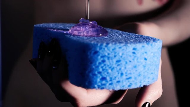 Naked fit woman holding in hand blue shower sponge and poured gel, slow motion concept. Only hands. Bathroom routine, advertising of body washing cosmetic. Pouring liquid soap close up isolated