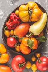 Different types of tomatoes and peppers on dark background, top view.