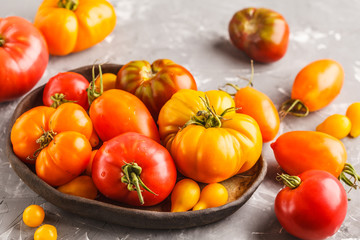 Different types of tomatoes in dark plate, dark background.