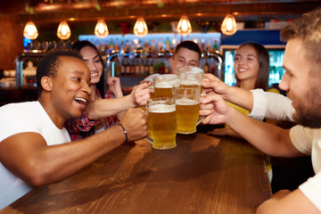 Group of happy friends enjoying beer at pub, toasting and laughing.
