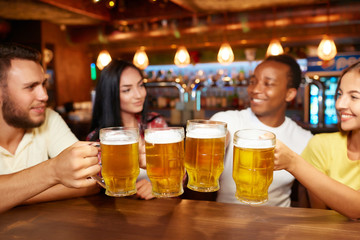 Four friends toasting with glasses of light beer at pub.