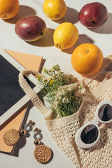 top view of digital tablet, earrings, sunglasses, flowers and string bag with fresh ripe fruits