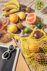 top view of digital tablet, sunglasses and yellow string bag with fresh ripe tropical fruits