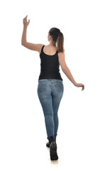 full length portrait of brunette girl wearing black single and jeans. standing pose with back to the camera. isolated on white studio background.