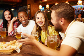 Company of friends sitting in bar and drinking beer with snacks.