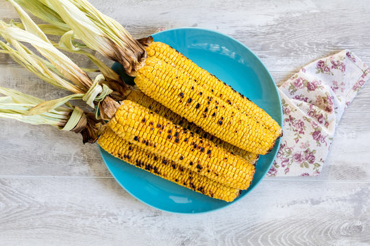 Corn baked in olive oil and salt on blue dish on light surface