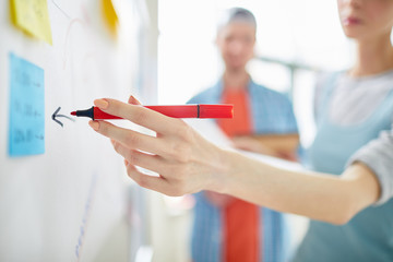 Close-up of professional manager drawing with marker pen on whiteboard while offering marketing strategy at meeting