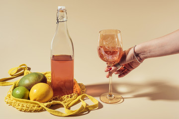 cropped shot of person holding glass with beverage, bottle and string bag with fruits on brown
