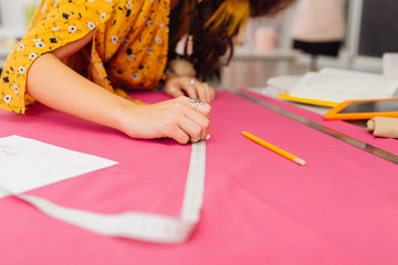 Tape measure. Careful experienced dressmaker holding a piece of chalk and a tape measure while drawing the line on pink fabric