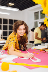 Fototapeta premium Necessary procedure. Cheerful enthusiastic young dressmaker feeling satisfied with her work and smiling while using a tape measure