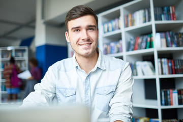 Portrait of smiling teenager sitting and doing homework at library