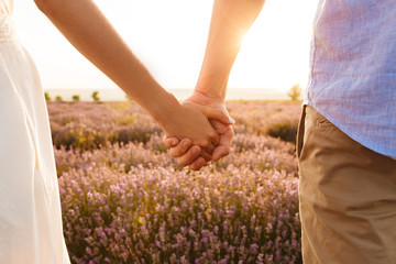 Cropped image from back of young couple man and woman holding hands, while walking outdoor in lavender field