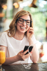 Woman texting and listening music on the mobile phone in the cafe
