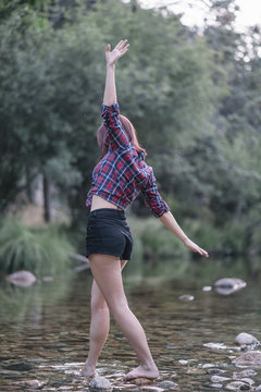 Pretty red haired girl performs exercises by the river.